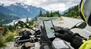 Close-up photorealistic illustration showing conductive fiber patch technology on black motorcycle gloves for precise smartphone use, with a scenic Canadian mountain background.